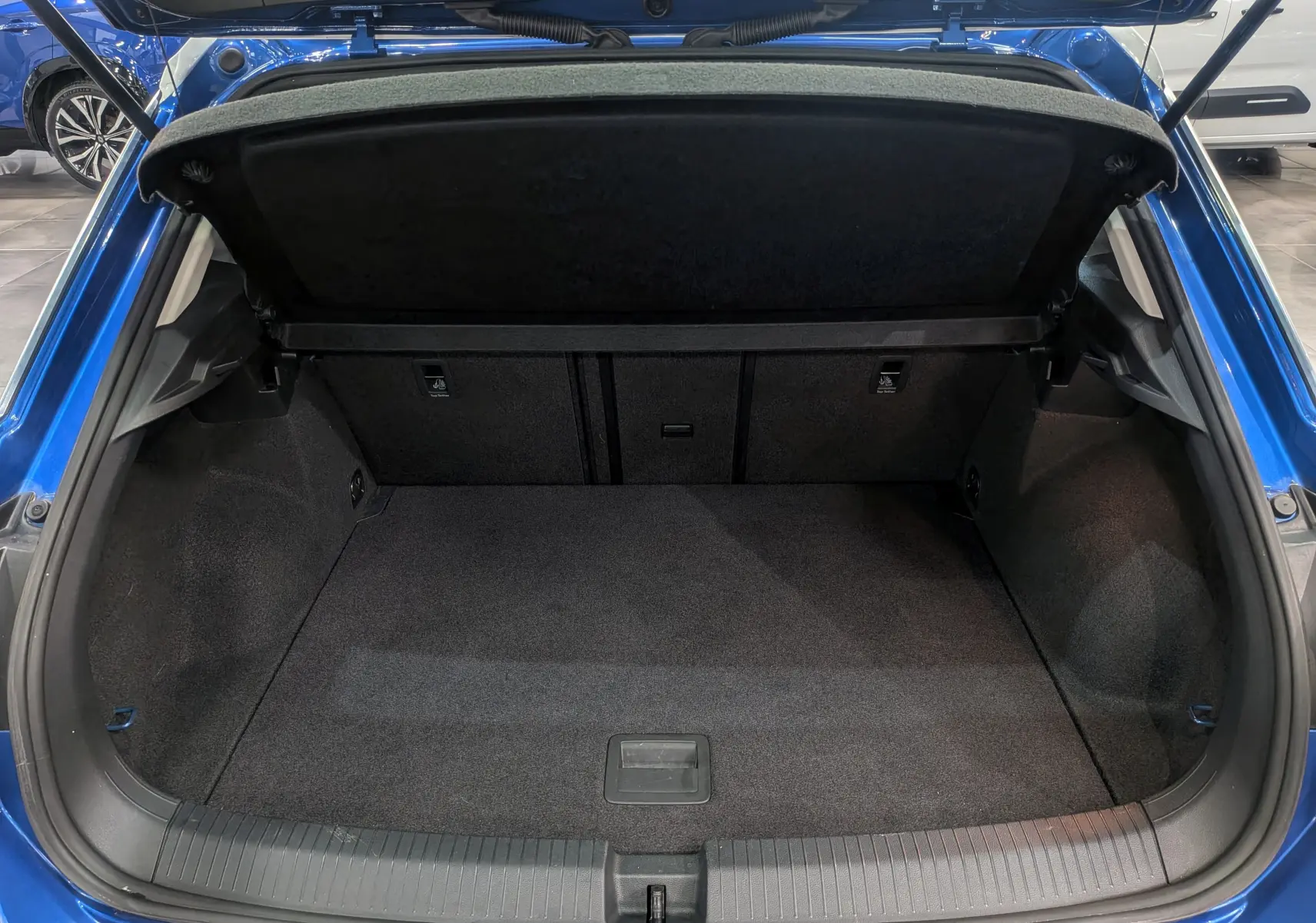 Coffre ouvert du Volkswagen T-Roc bleu Ravenna avec toit blanc, vue arrière montrant l'espace de chargement vide.