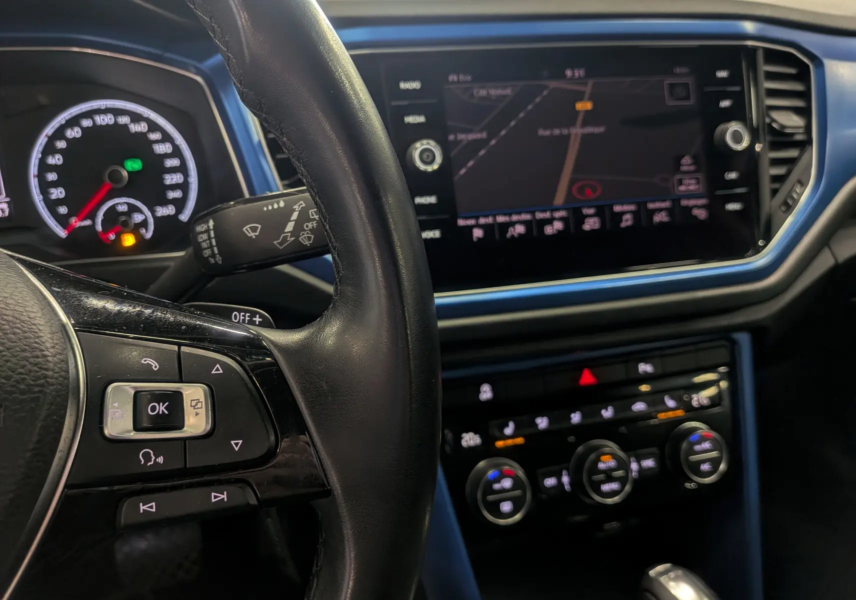Vue rapprochée du tableau de bord bleu du Volkswagen T-Roc 2018, avec volant et écran tactile affichant la navigation.