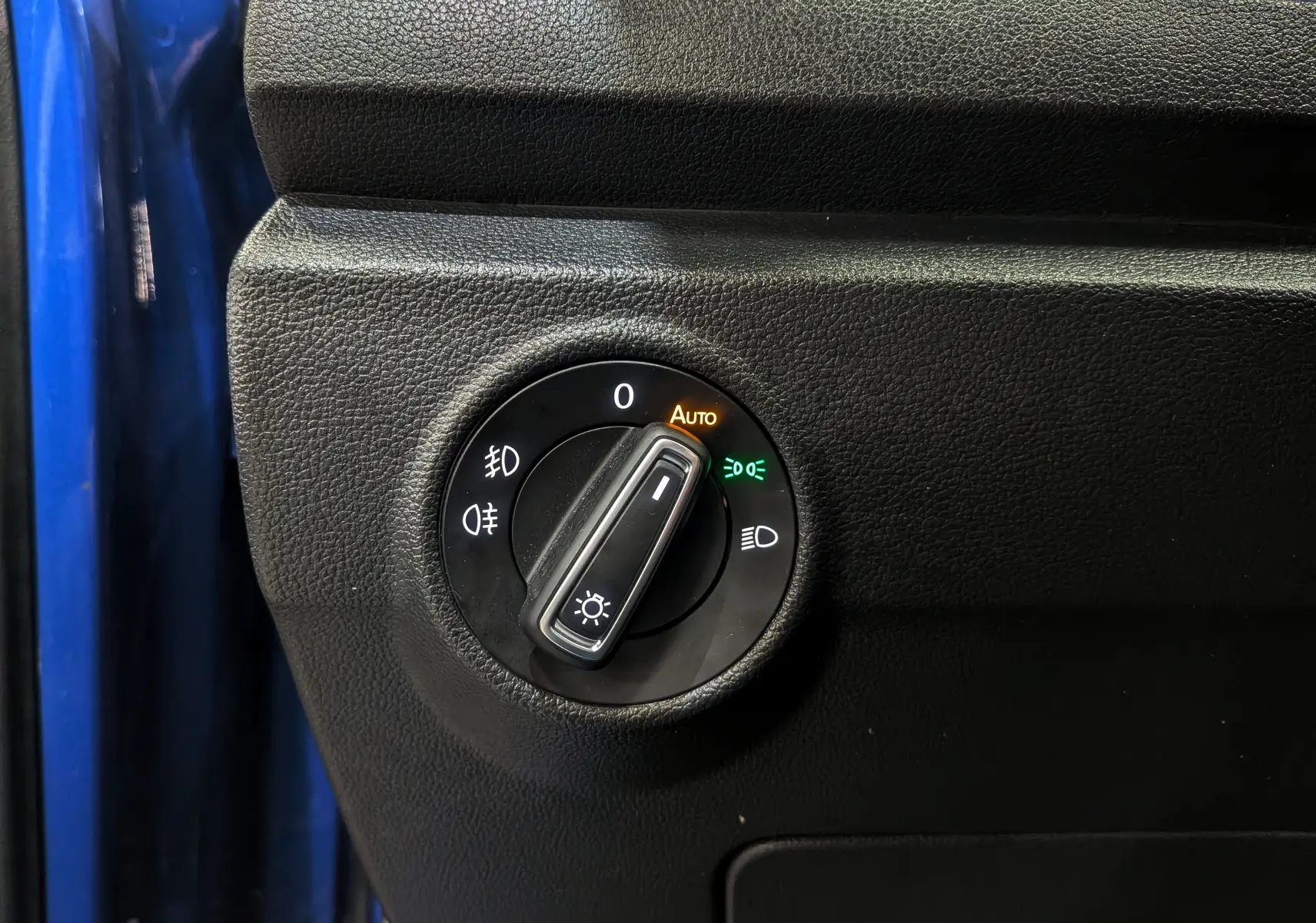 Gros plan sur le bouton de réglage des phares du Volkswagen T-Roc bleu Ravenna, avec fonction automatique activée.