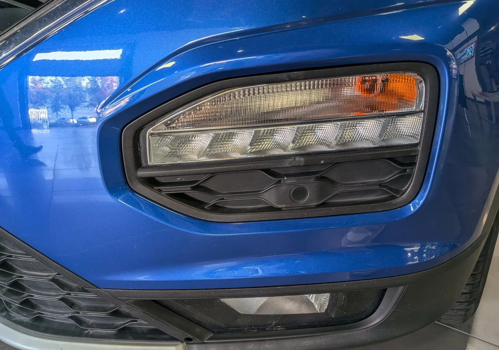 Gros plan sur le phare avant droit du Volkswagen T-Roc bleu Ravenna avec détails noirs et clignotant orange.