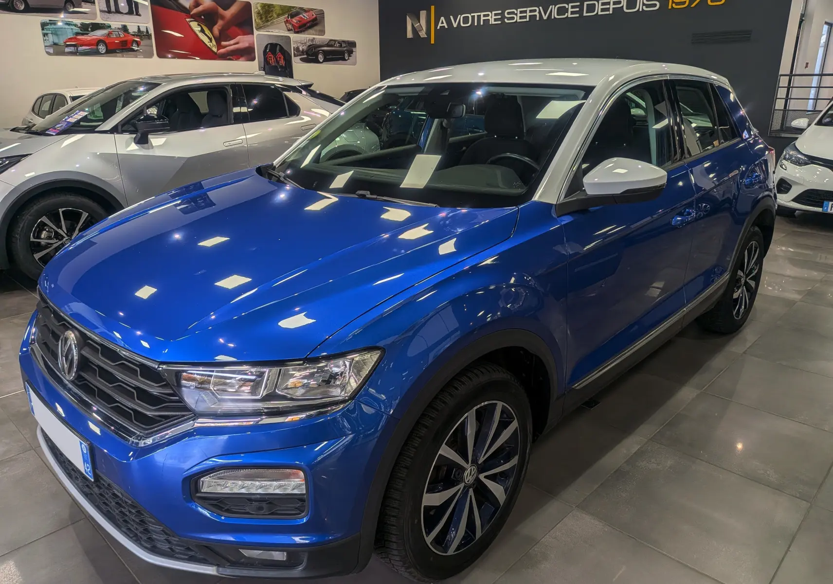 Volkswagen T-Roc bleu Ravenna avec toit blanc, vue 3/4 avant droit, en showroom lumineux.