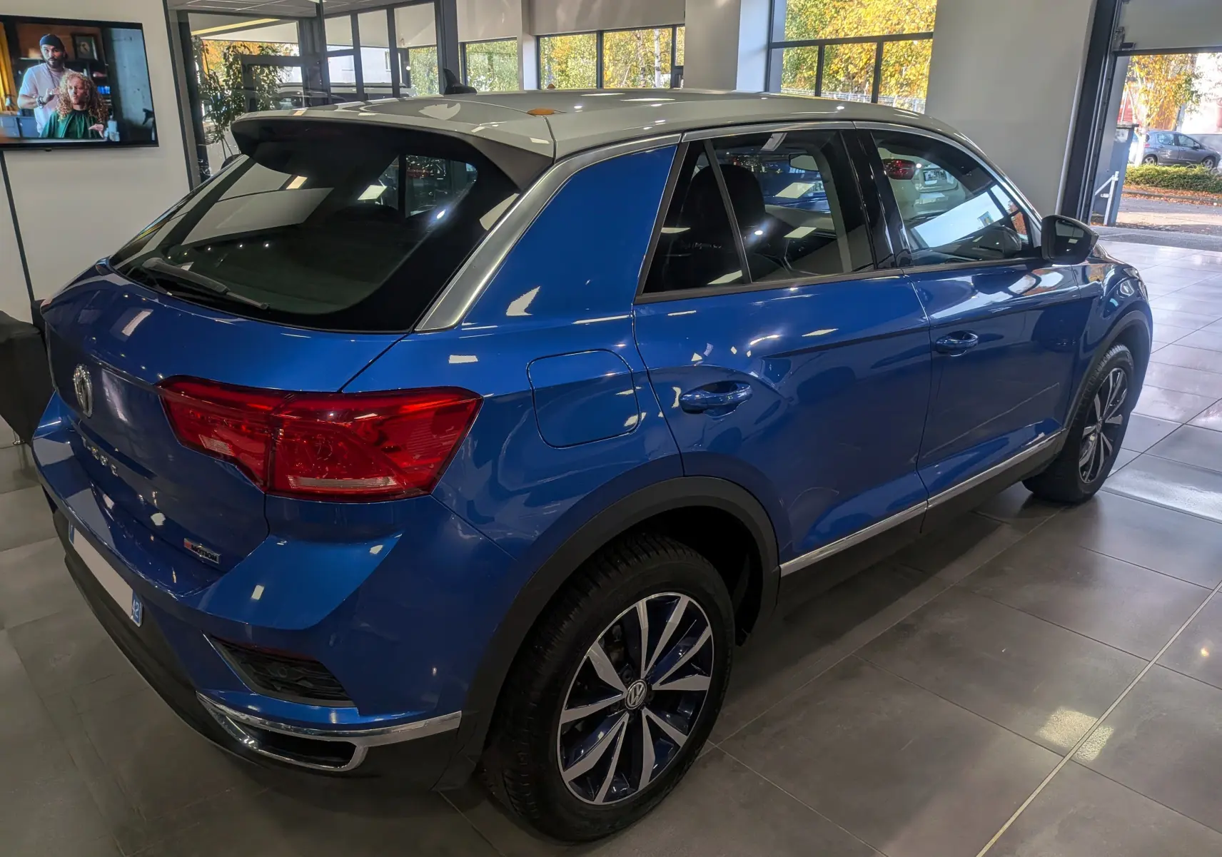 Volkswagen T-Roc bleu Ravenna avec toit blanc, vue 3/4 arrière droit en intérieur de showroom.