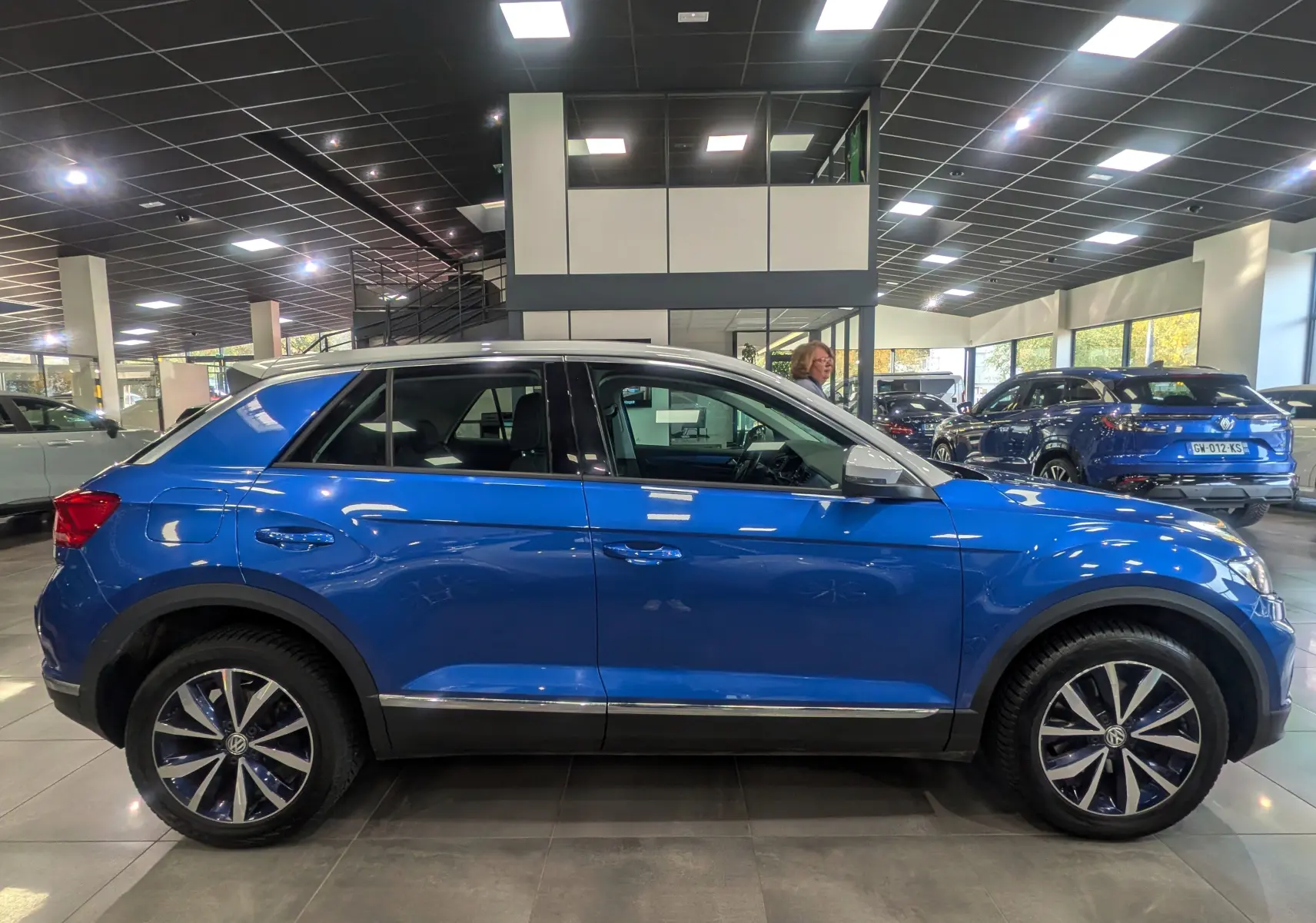 Profil côté gauche du Volkswagen T-Roc 2018 bleu Ravenna avec toit blanc, en intérieur de showroom.