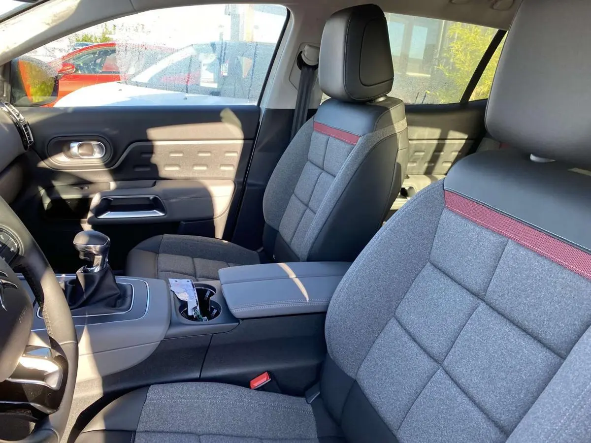 Intérieur avant du Citroën C5 Aircross blanc 2021, sièges gris avec inserts rouges et volant cuir noir.