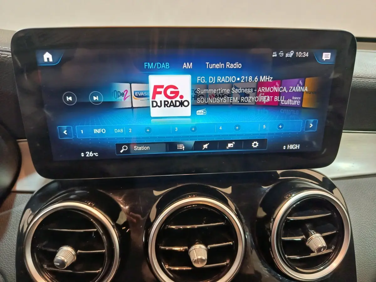 Écran tactile central allumé avec radio FM, entouré de trois aérateurs ronds dans l’habitacle du Mercedes GLC bleu.