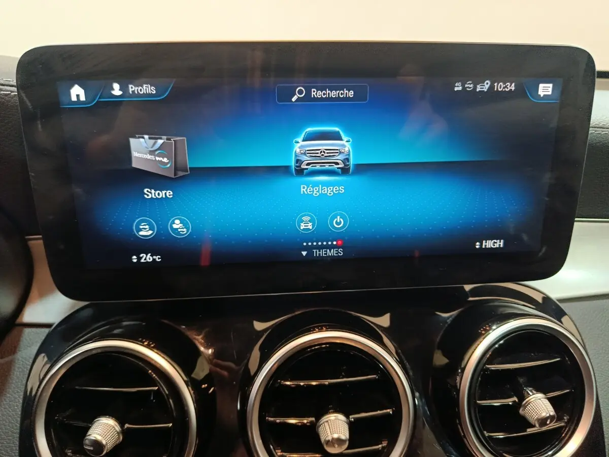 Écran tactile central affichant le menu Réglages sur le tableau de bord du Mercedes GLC 300 E bleu, avec aérateurs ronds chromés.