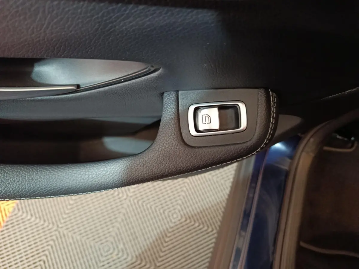 Gros plan sur la commande de lève-vitre côté conducteur, garniture cuir noire et bord bleu métallisé visible.