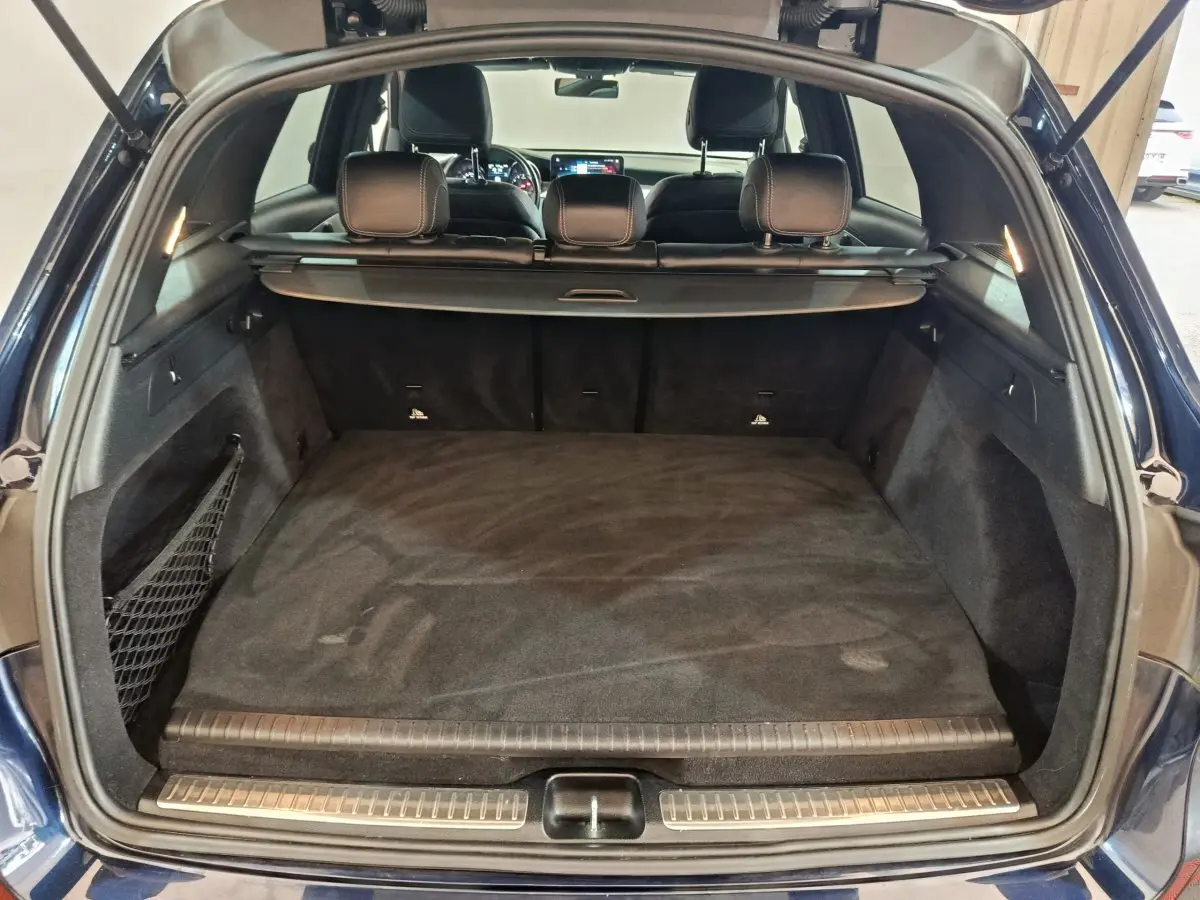 Coffre ouvert d'un Mercedes GLC 300 E bleu, vue arrière montrant l'espace de chargement et la banquette arrière.