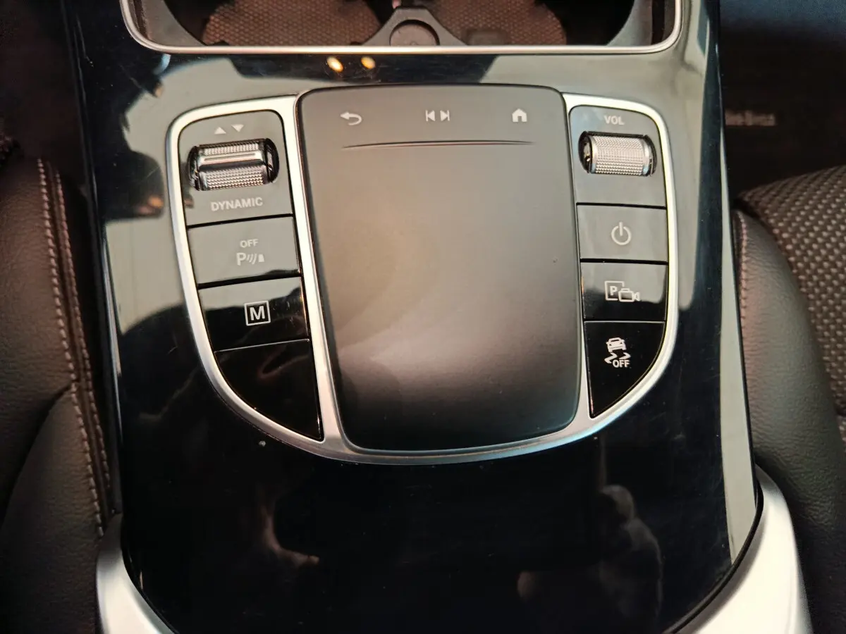 Gros plan sur la console centrale noire brillante avec pavé tactile et commandes du Mercedes GLC 300 E bleu hybride rechargeable.