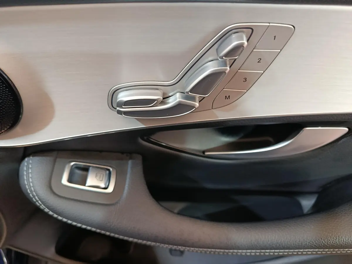 Détail des commandes de réglage de siège en aluminium brossé sur la porte côté gauche d’un Mercedes GLC bleu 2021.