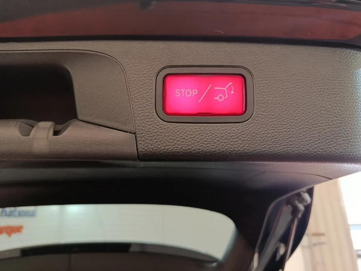 Bouton rouge d'arrêt électrique du coffre visible sur le bord intérieur du hayon d'un Mercedes GLC bleu hybride rechargeable.