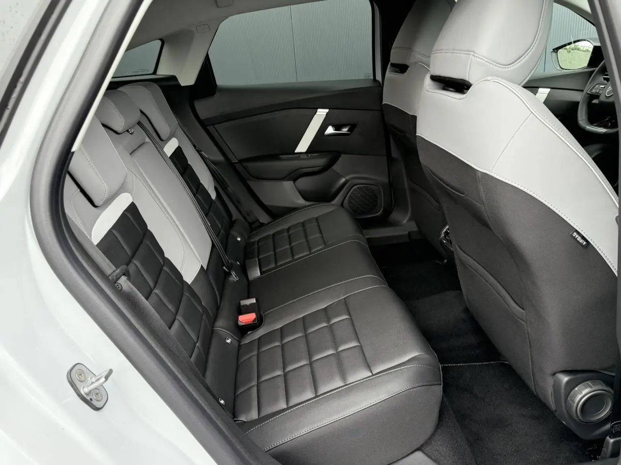 Vue intérieure arrière côté gauche montrant les sièges arrière bicolores noir et gris du Citroën C4 hybride 2025.