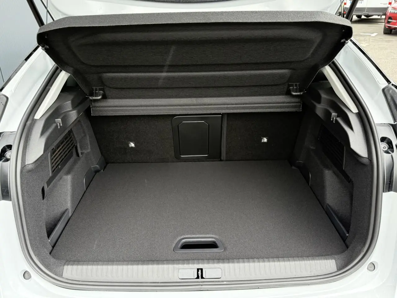 Coffre ouvert vu de l'arrière d'une Citroën C4 hybride blanche avec intérieur noir et cache-bagages relevé.