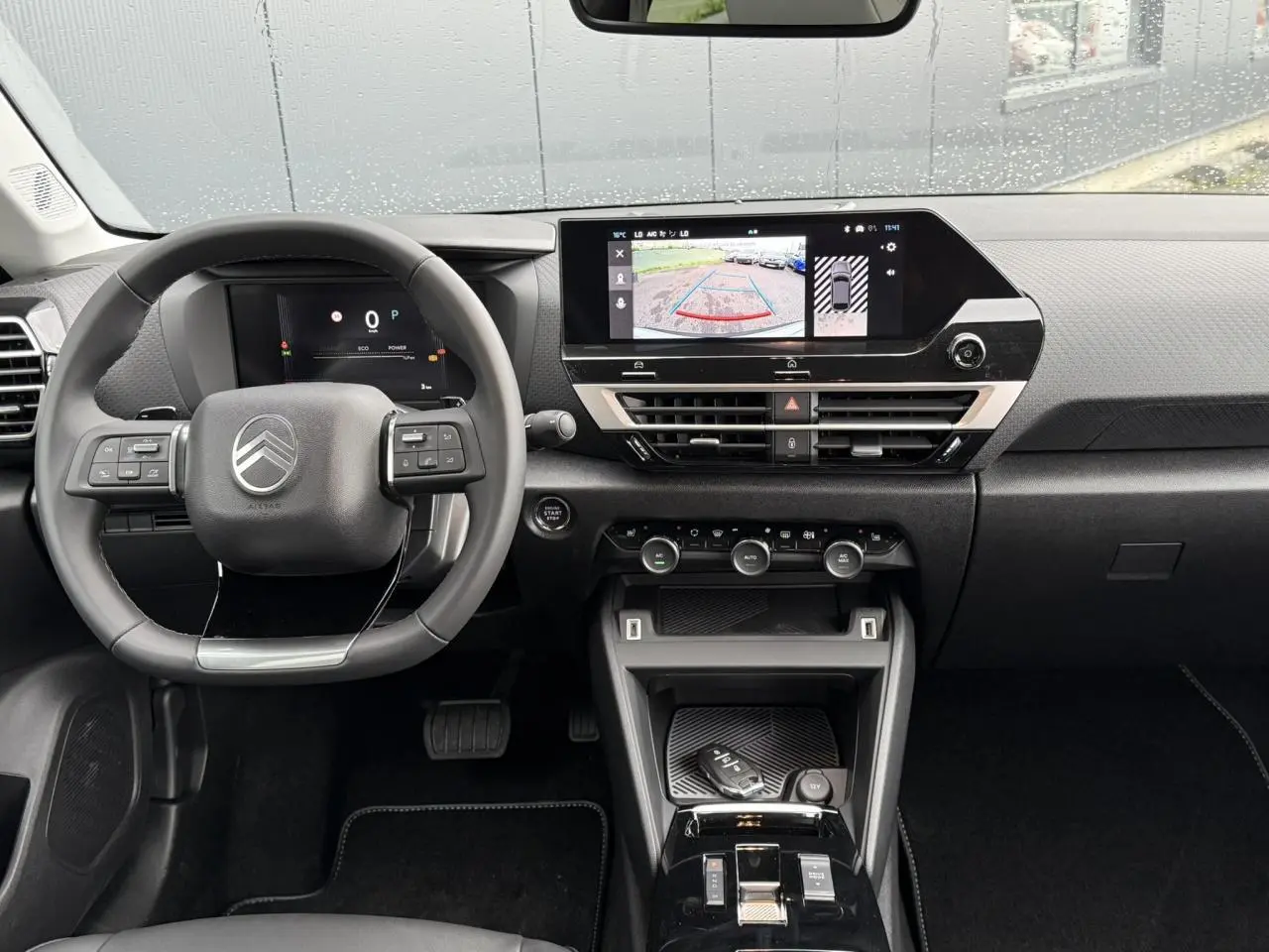 Vue intérieure avant du tableau de bord et volant de la Citroën C4 hybride 2025 avec écran tactile affichant la caméra de recul.