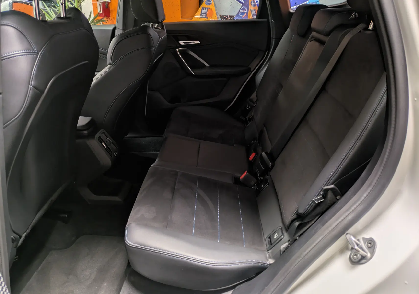 Vue intérieure côté droit des sièges arrière en cuir noir et alcantara avec surpiqûres bleues du BMW X1 blanc 2025 M SPORT.