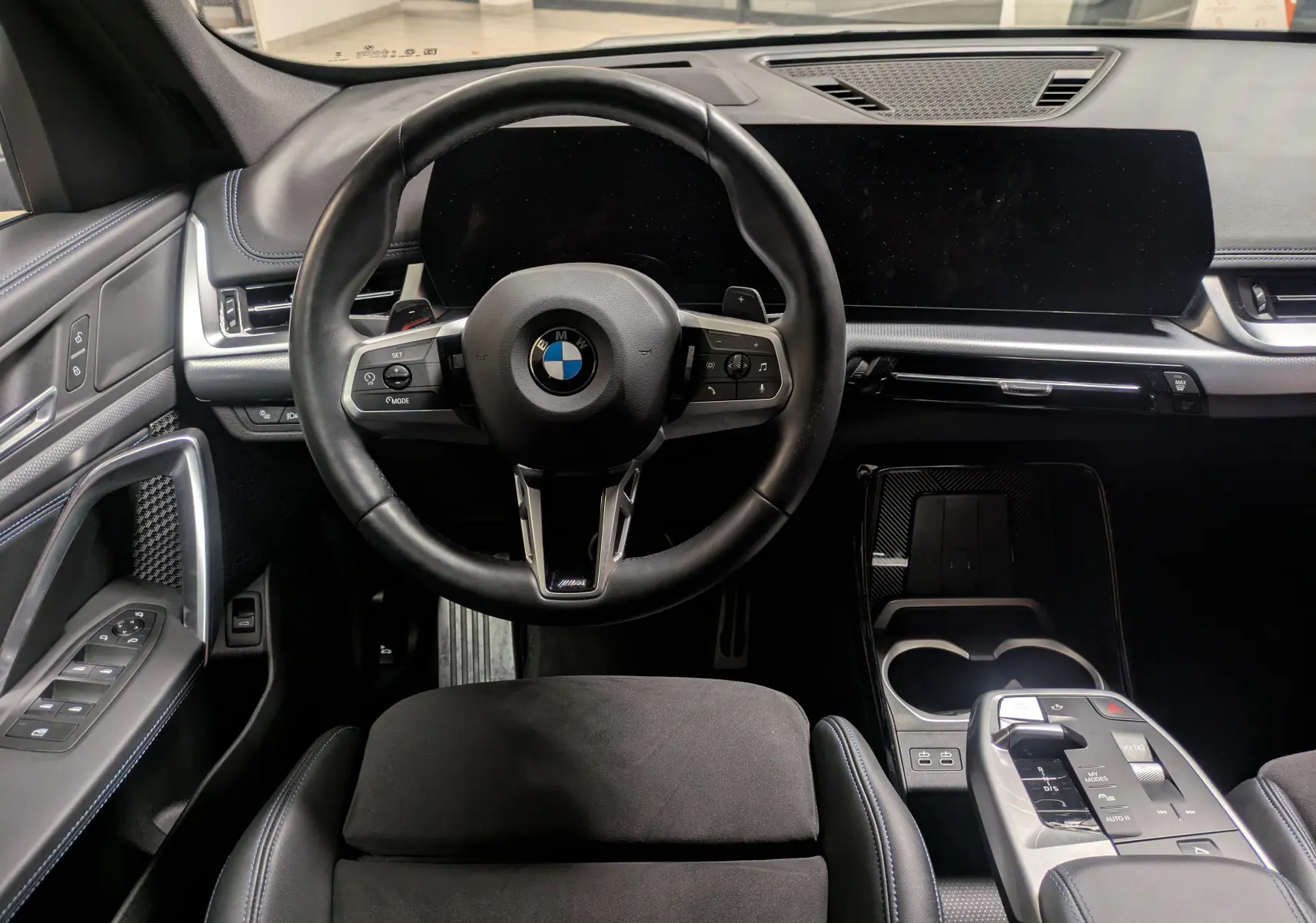 Vue intérieure centrée sur le volant cuir M et le tableau de bord numérique du BMW X1 blanc 2025.