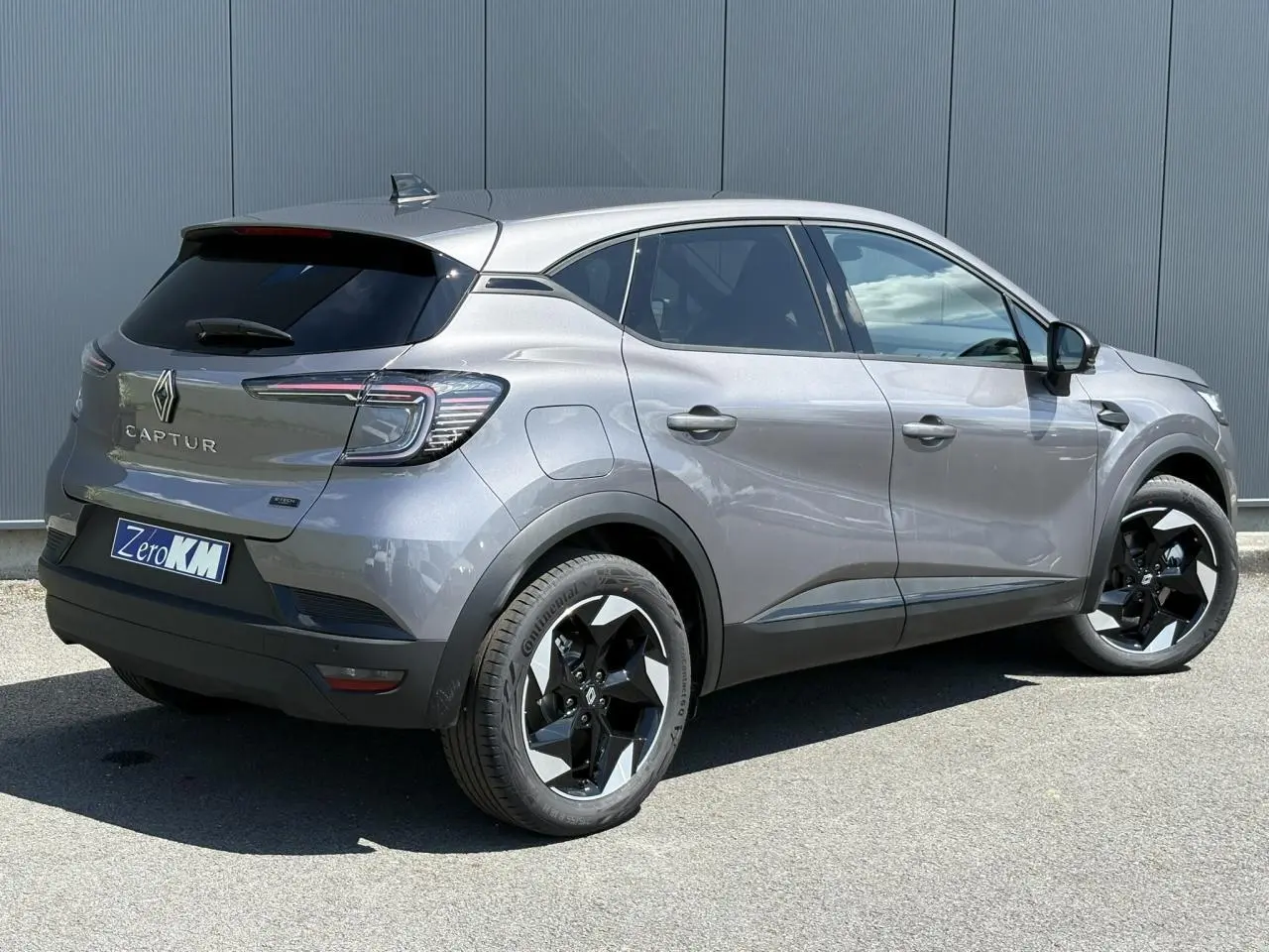 Renault Captur gris Cassiopée en 3/4 arrière droit, jantes noires et feux arrière LED distinctifs visibles.