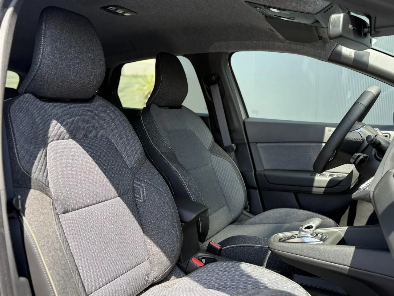 Vue intérieure côté conducteur du Renault Captur 2025 gris Cassiopée, sièges tissu gris et volant cuir multifonctions.