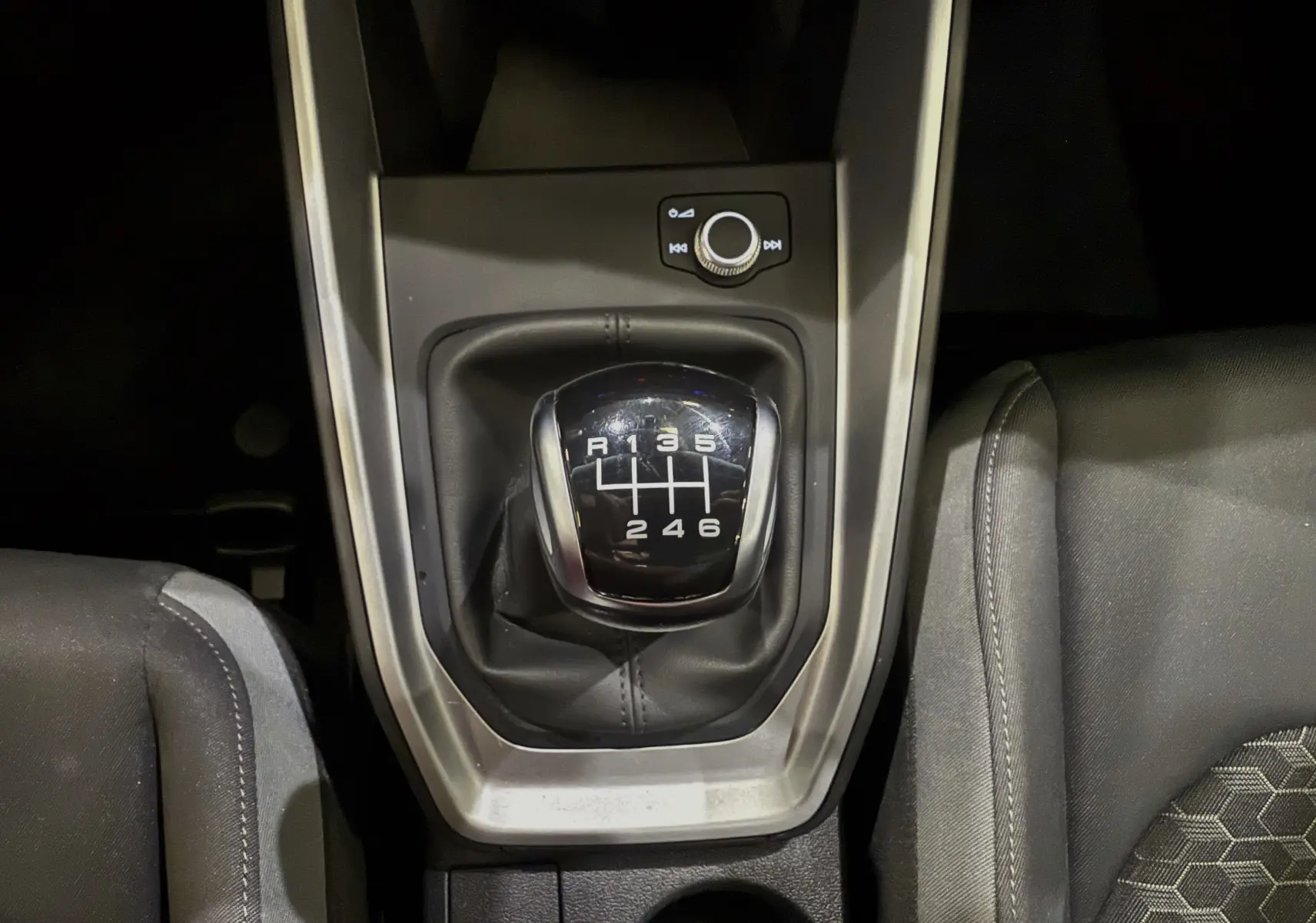 Le levier de vitesses manuel 6 rapports de l'Audi A1 30 TFSI S-Line 2024, entouré de sièges en tissu noir.