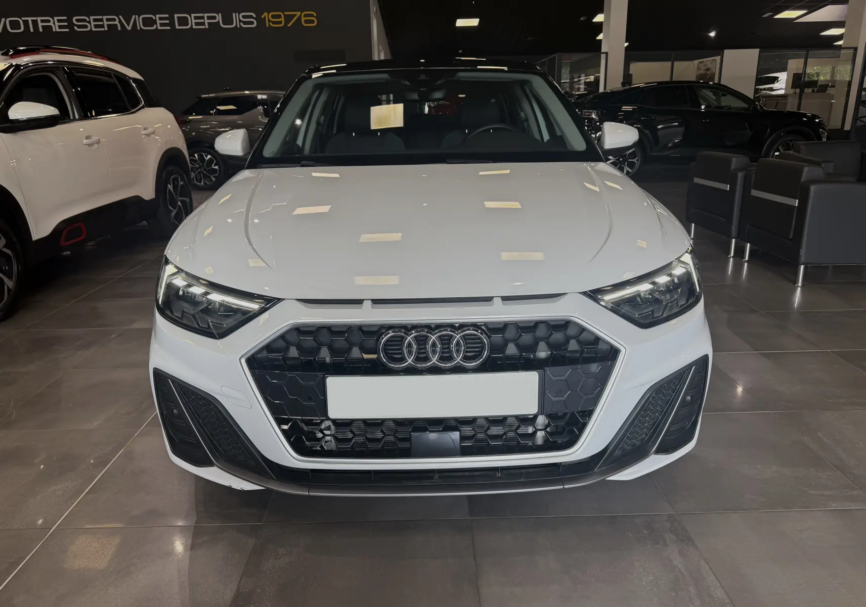 Audi A1 30 TFSI blanche avec toit noir vue de face en intérieur, calandre hexagonale et phares LED distinctifs.