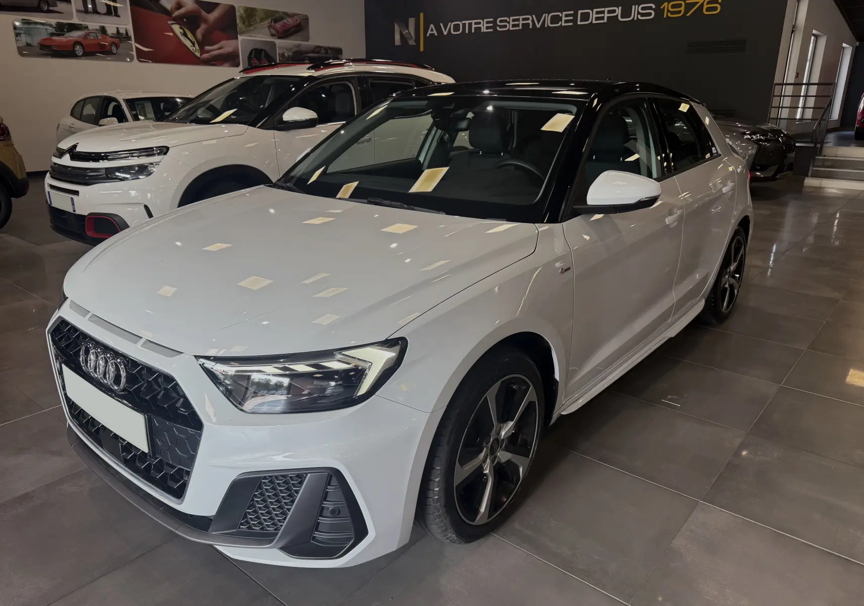 Audi A1 30 TFSI S-Line blanche avec toit noir, vue 3/4 avant droit en intérieur de showroom.