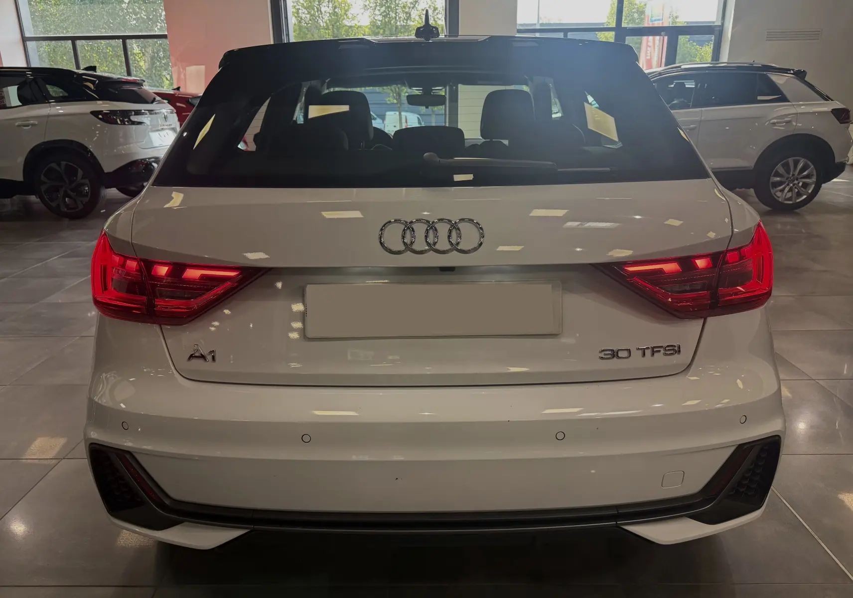 Vue arrière d'une Audi A1 blanche avec toit noir, feux LED allumés, en intérieur de showroom.