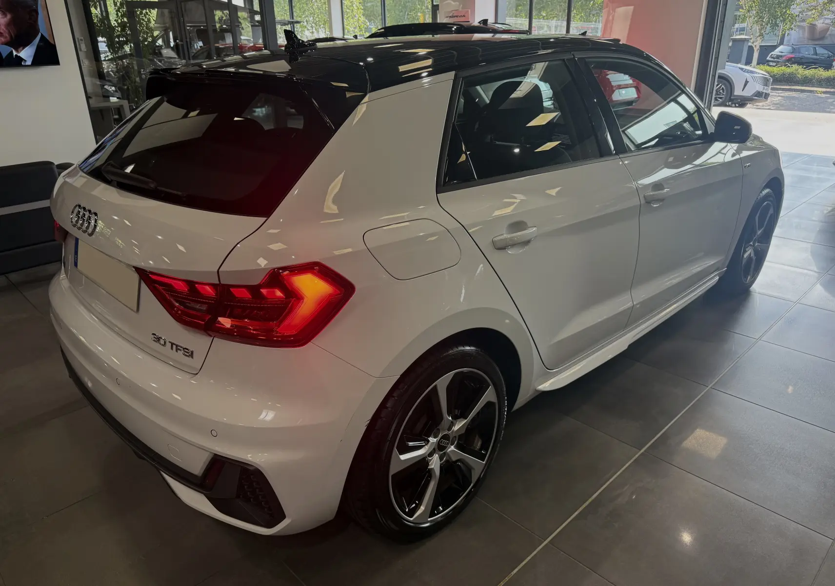 Audi A1 30 TFSI S-Line blanche avec toit noir, vue 3/4 arrière droit en showroom lumineux.