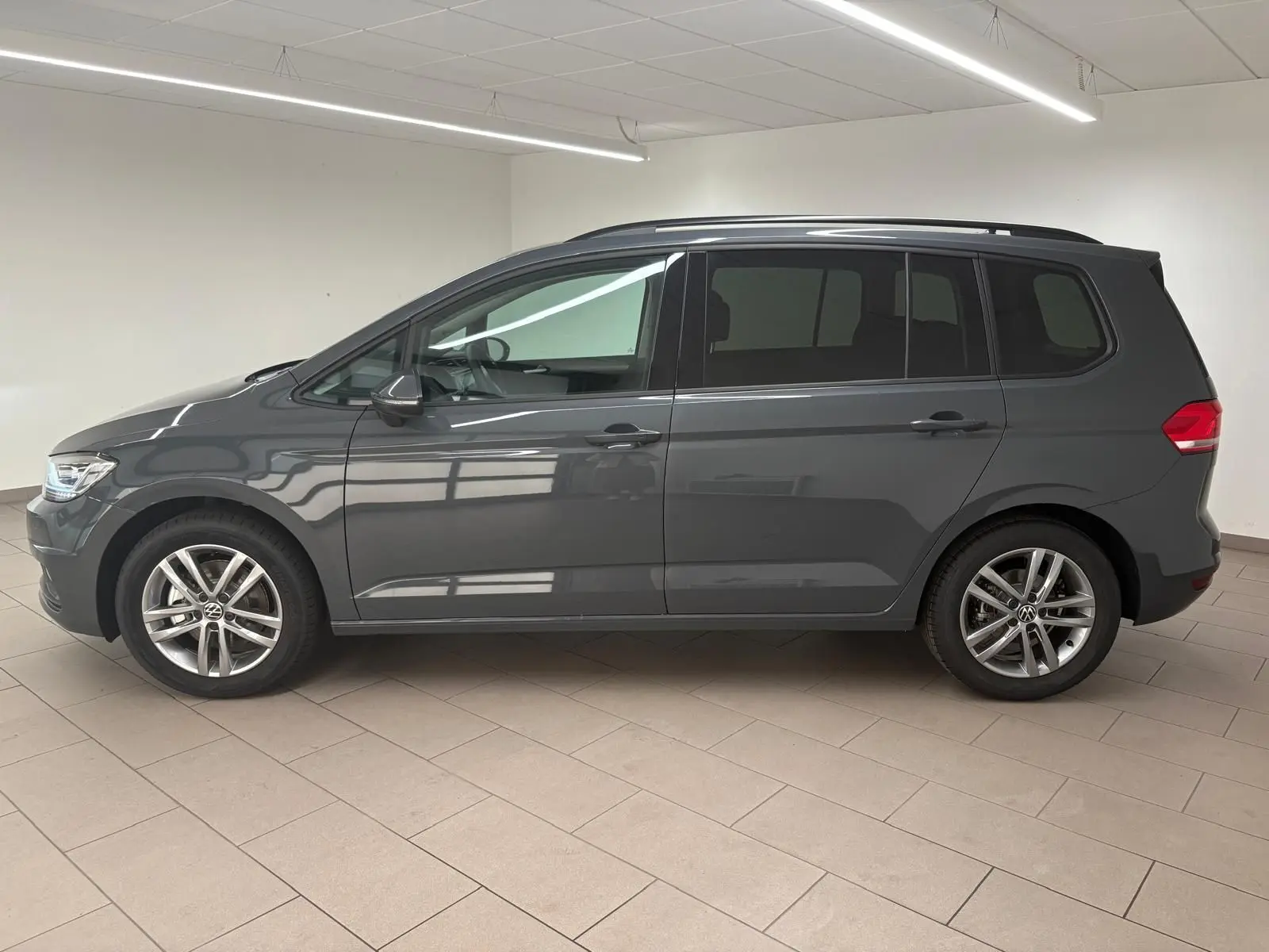 Profil côté gauche d'un Volkswagen Touran 2025 gris dauphin avec jantes alliage 17 pouces en intérieur lumineux.