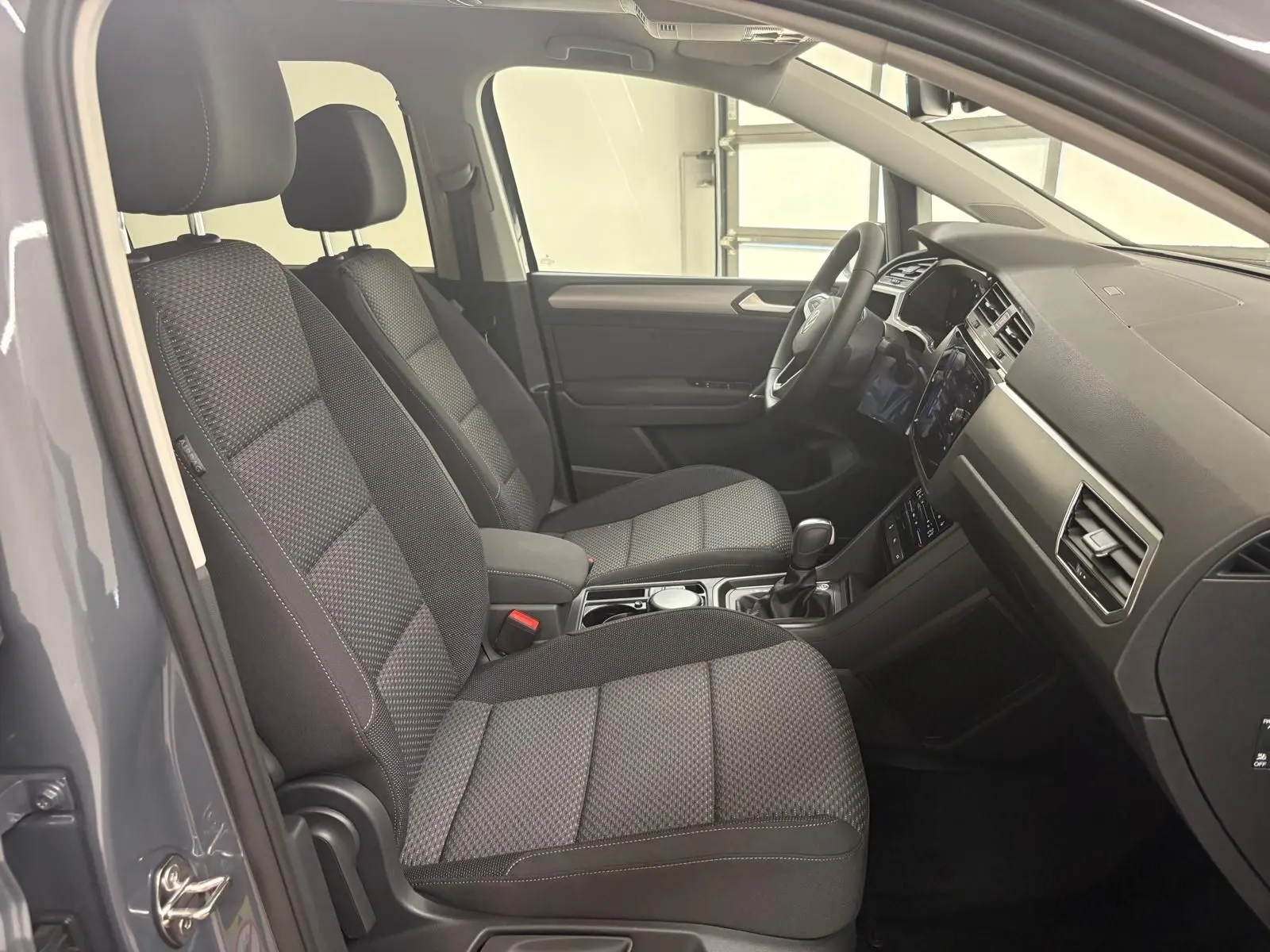 Intérieur du Volkswagen Touran 2025 gris dauphin, vue côté gauche sur les sièges avant et tableau de bord moderne.