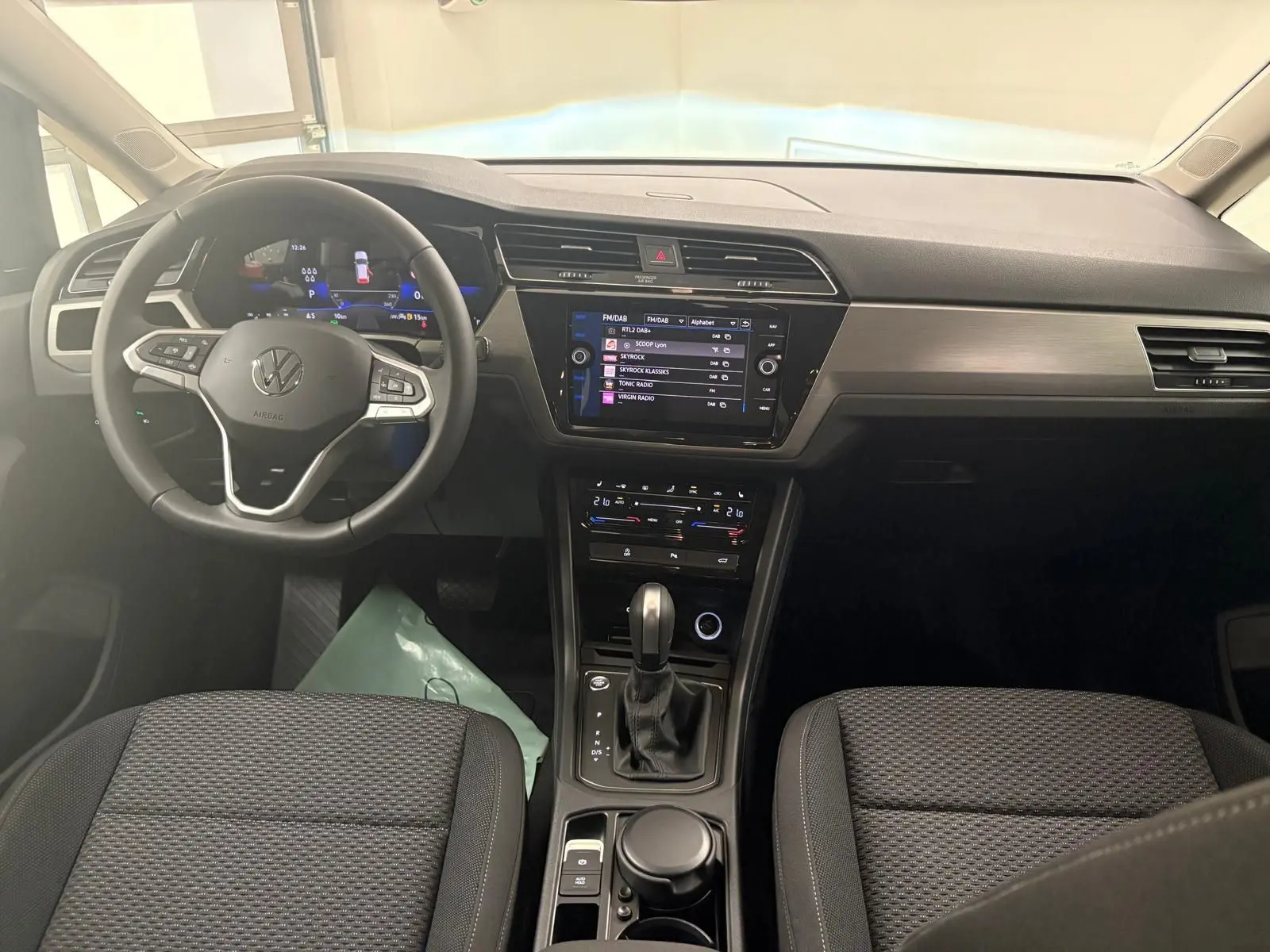 Vue intérieure frontale du tableau de bord et volant du Volkswagen Touran gris dauphin avec écran tactile et console centrale moderne.