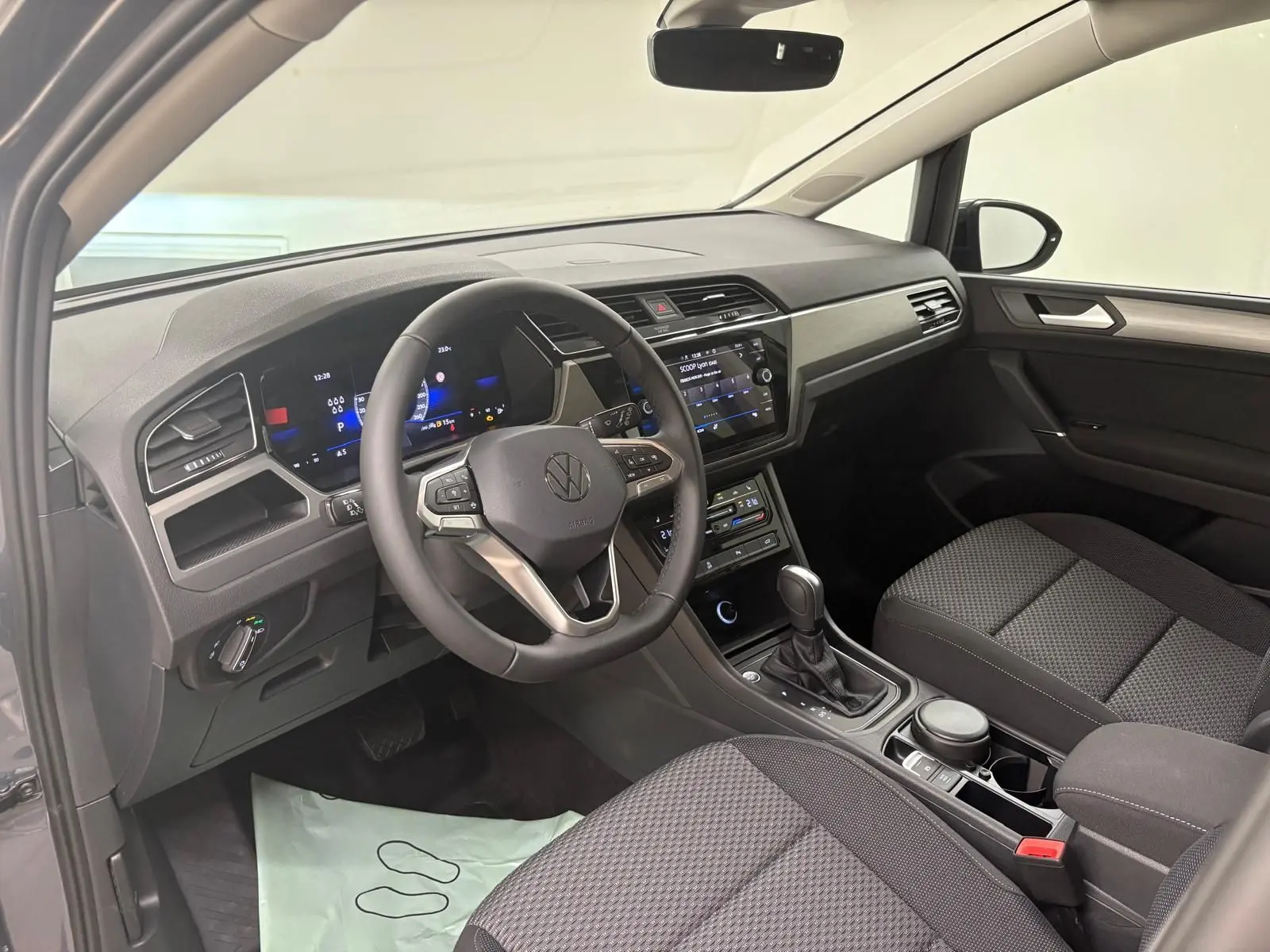 Intérieur avant droit du Volkswagen Touran gris Dauphin 2025, tableau de bord moderne avec écran tactile et volant multifonction.