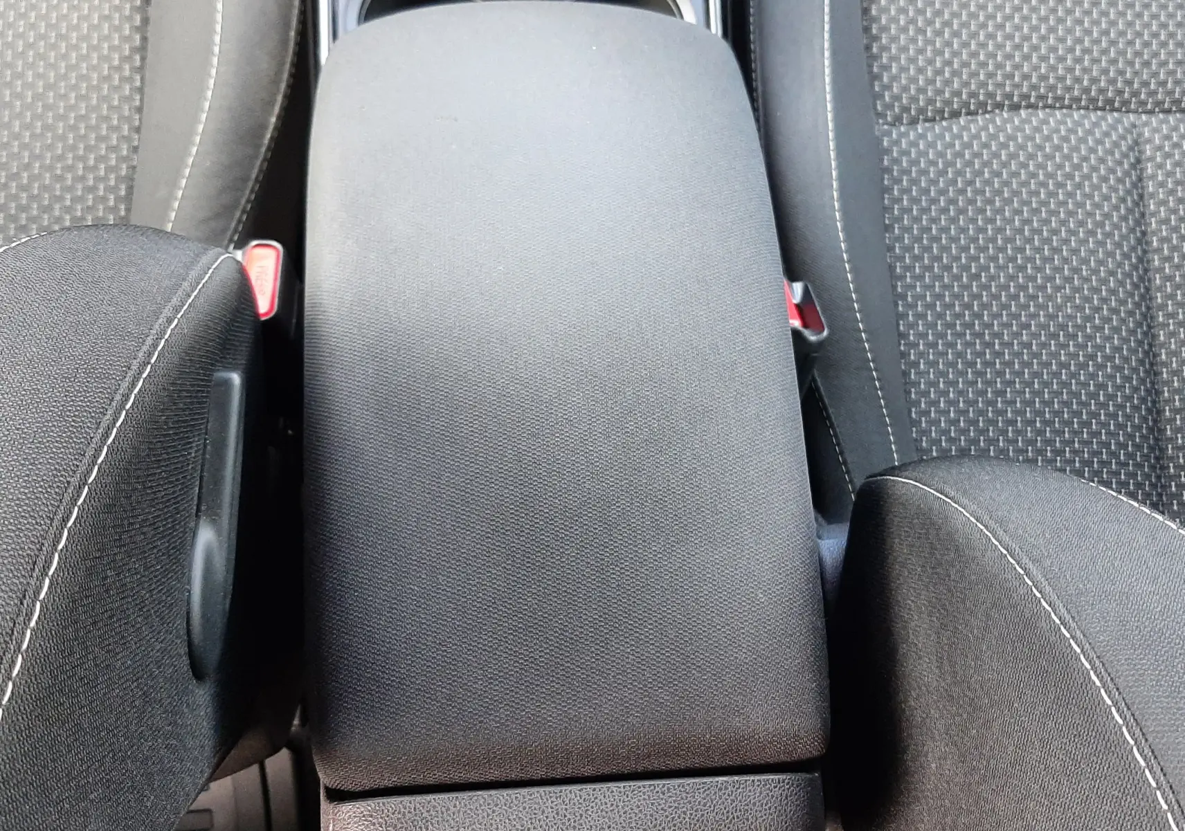 Vue plongeante sur l'accoudoir central noir et les sièges en tissu gris du Renault Kadjar 1.5 dCi 2018.