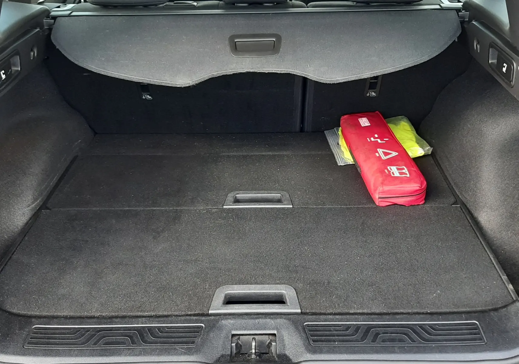 Coffre ouvert du Renault Kadjar gris 2018 vu de l'arrière, avec cache-bagages et trousse de secours rouge à droite.