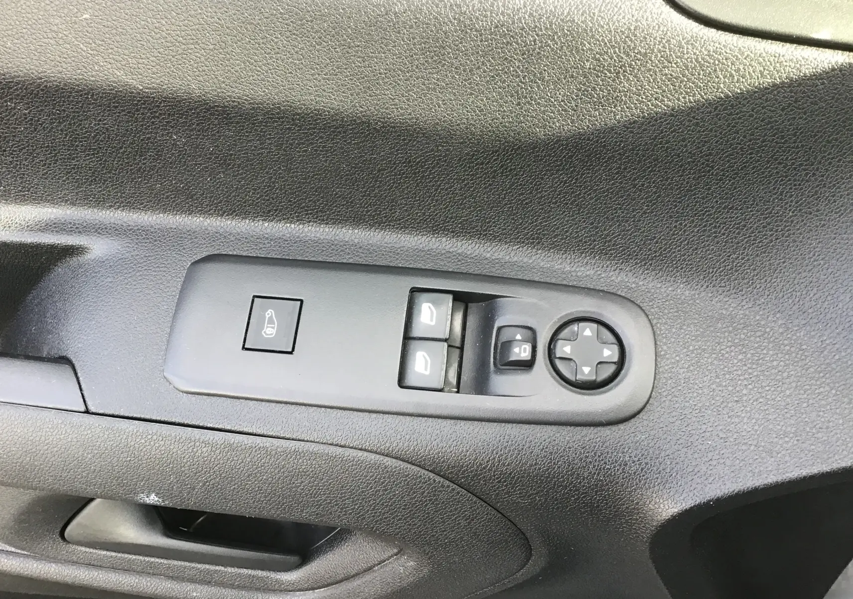 Gros plan sur les commandes de lève-vitres et réglage des rétroviseurs côté conducteur d'un Citroën Berlingo blanc.