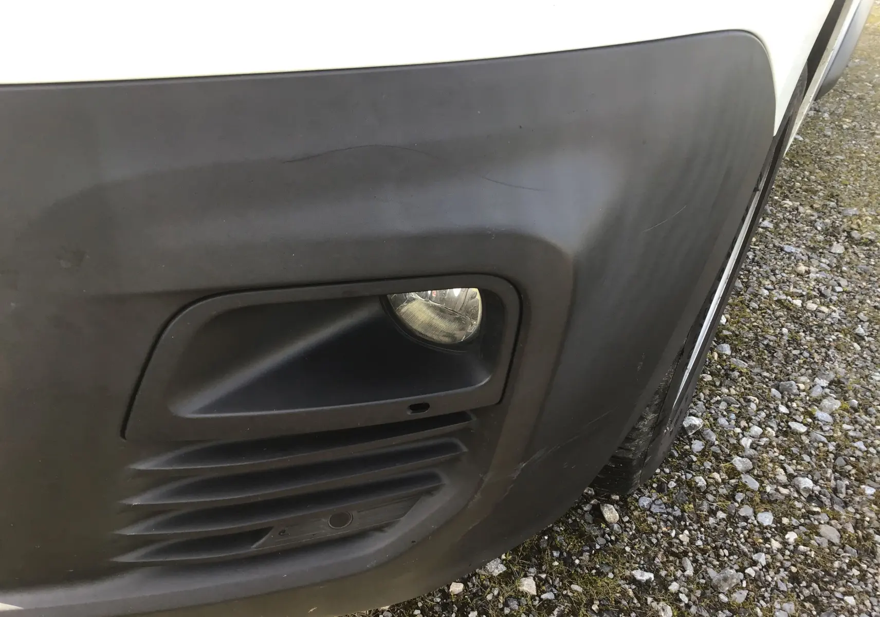 Gros plan sur le pare-chocs avant droit noir du Citroën Berlingo blanc, avec antibrouillard et capteur de stationnement visible.