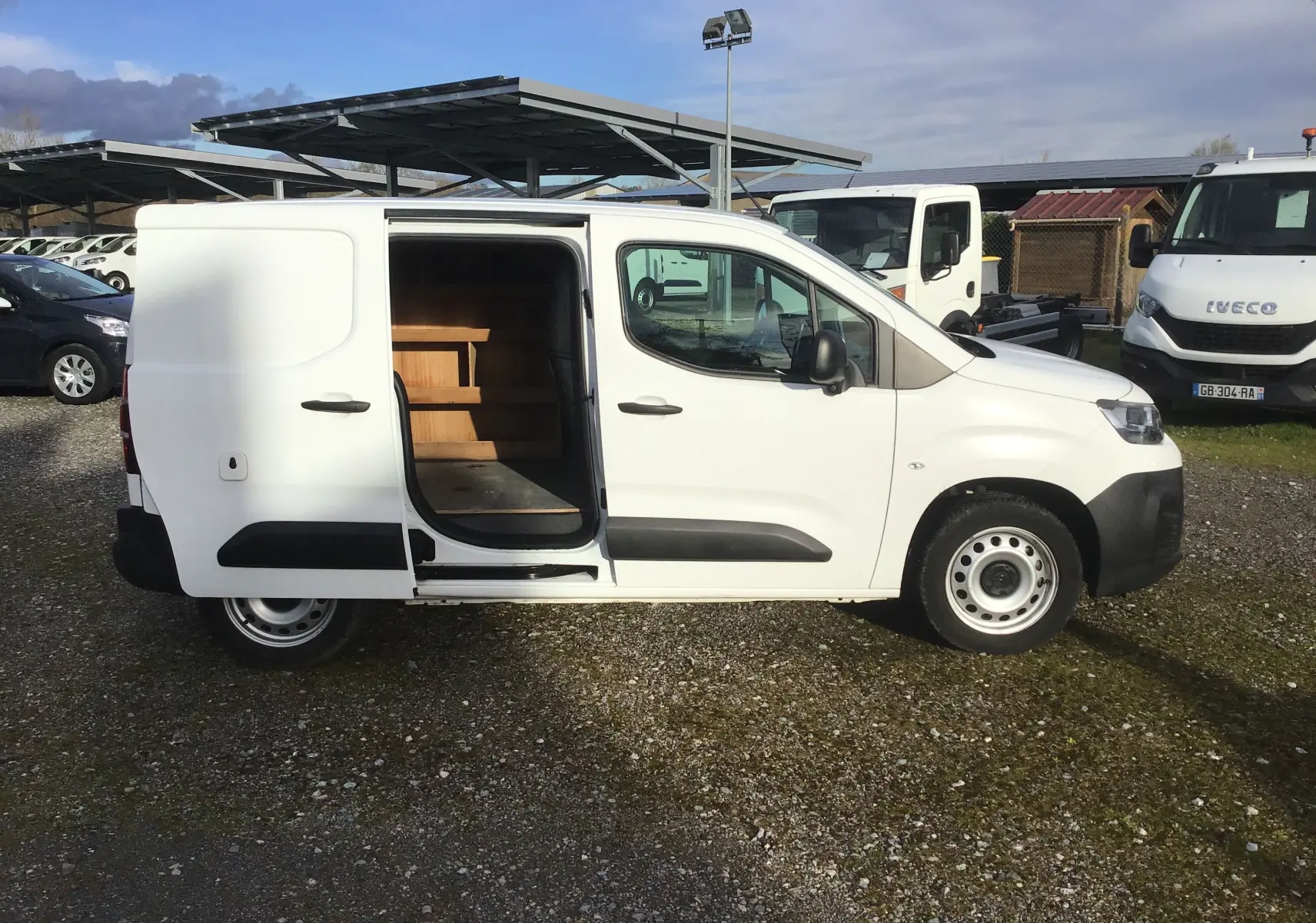 Vue de profil droit d’un utilitaire Citroën Berlingo blanc 2019 avec porte latérale coulissante ouverte montrant l’aménagement intérieur en bois.