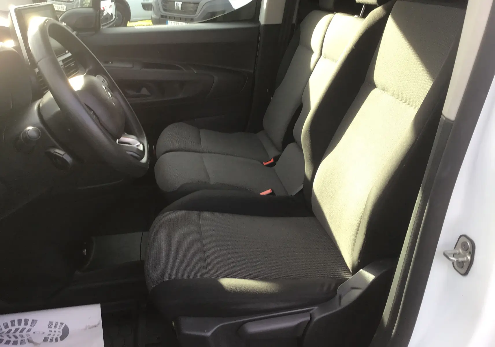 Vue intérieure côté conducteur du Citroën Berlingo blanc 2019, montrant les sièges avant en tissu gris foncé.