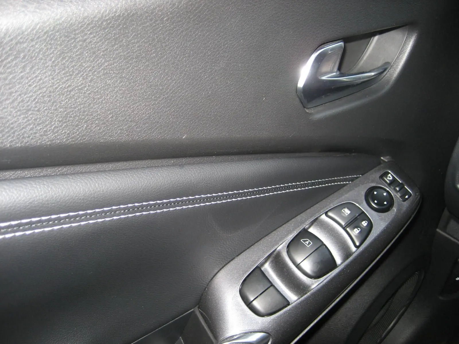 Gros plan sur la commande des vitres et rétroviseurs côté gauche du Nissan Juke 1.6 Hybrid 143 Tekna noir intérieur.