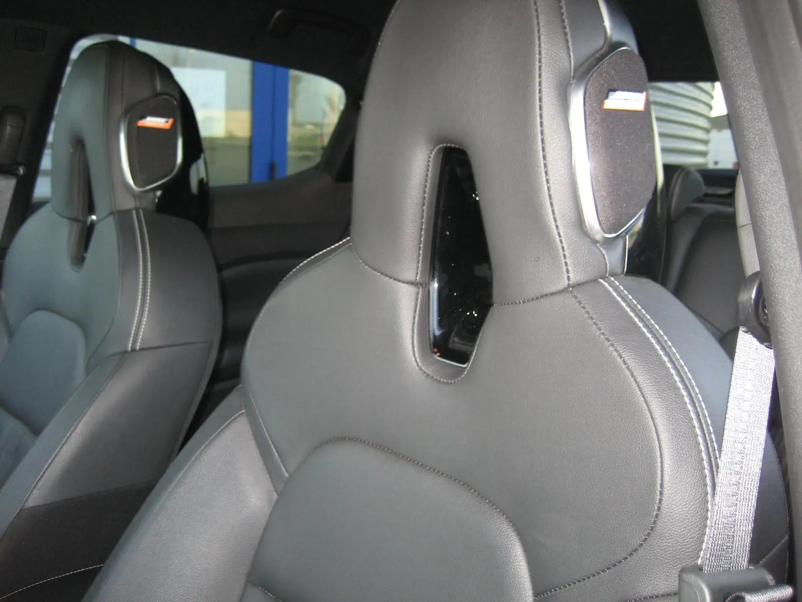 Gros plan sur les sièges avant en cuir noir du Nissan Juke 1.6 Hybrid 143 Tekna, soulignant les surpiqûres blanches et appuie-têtes intégrés.