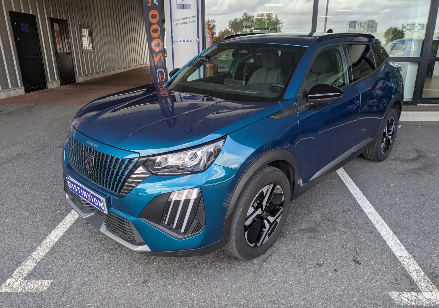 Peugeot 2008 Hybrid 145 bleu obsession en 3/4 avant droit, avec jantes alliage 17'' et barres de toit noir brillant.