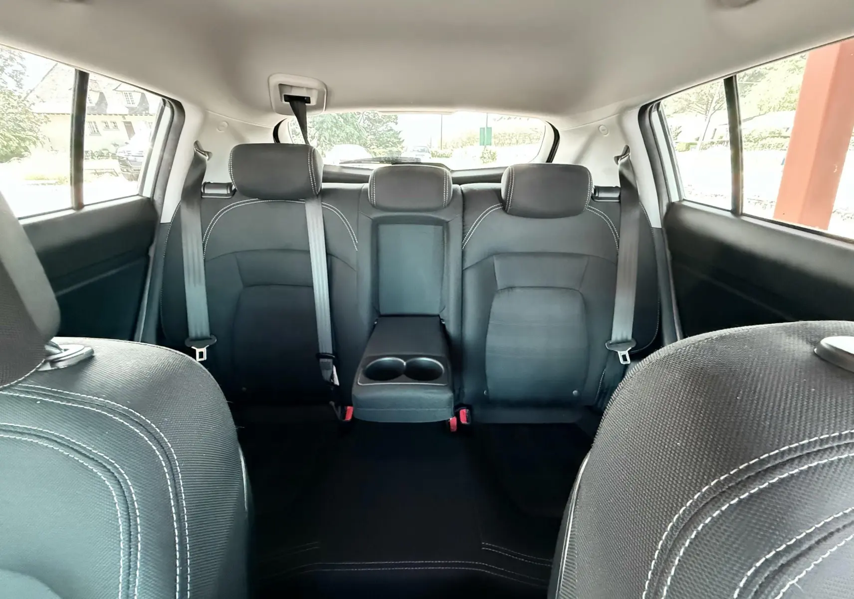 Vue intérieure arrière du Kia Sportage 2015, sièges noirs avec accoudoir central et ceintures visibles.