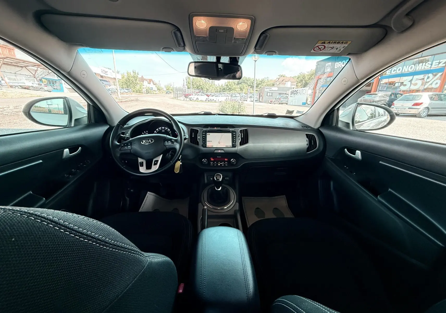 Vue intérieure avant du Kia Sportage 2015, tableau de bord noir avec volant multifonction et boîte manuelle.