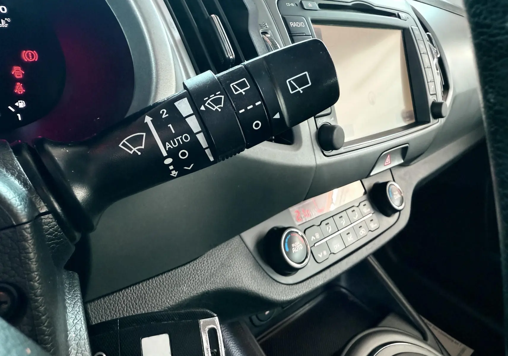 Gros plan sur la commande d’essuie-glace et le tableau de bord gris noir du Kia Sportage 2015 diesel blanc.