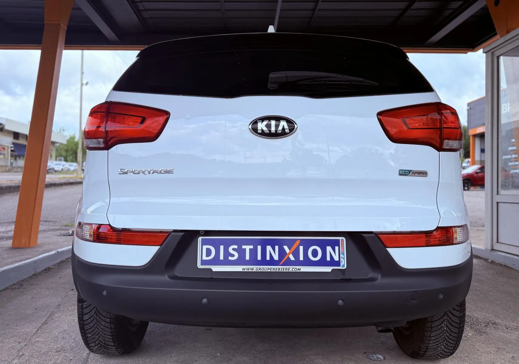 Vue arrière d'un Kia Sportage blanc 2015 avec feux rouges et plaque d'immatriculation Distinxion visible.