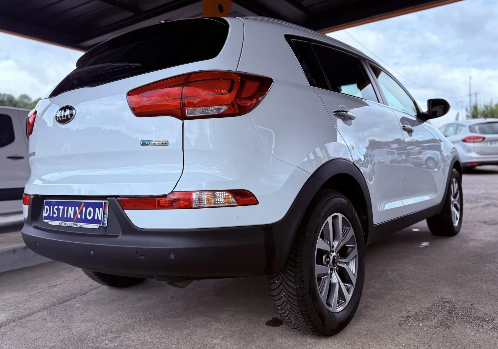 Vue 3/4 arrière droite d’un Kia Sportage blanc avec feux arrière rouges et jantes alliage sous abri.
