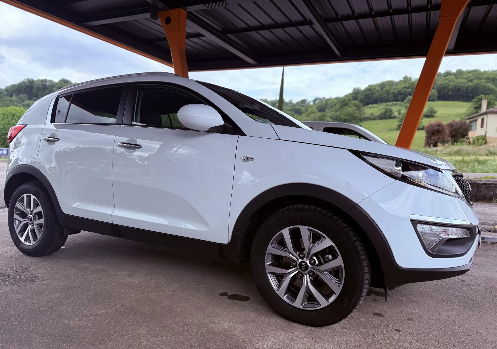 KIA Sportage blanche vue de profil côté droit sous abri avec jantes alliage et rétroviseurs blancs.