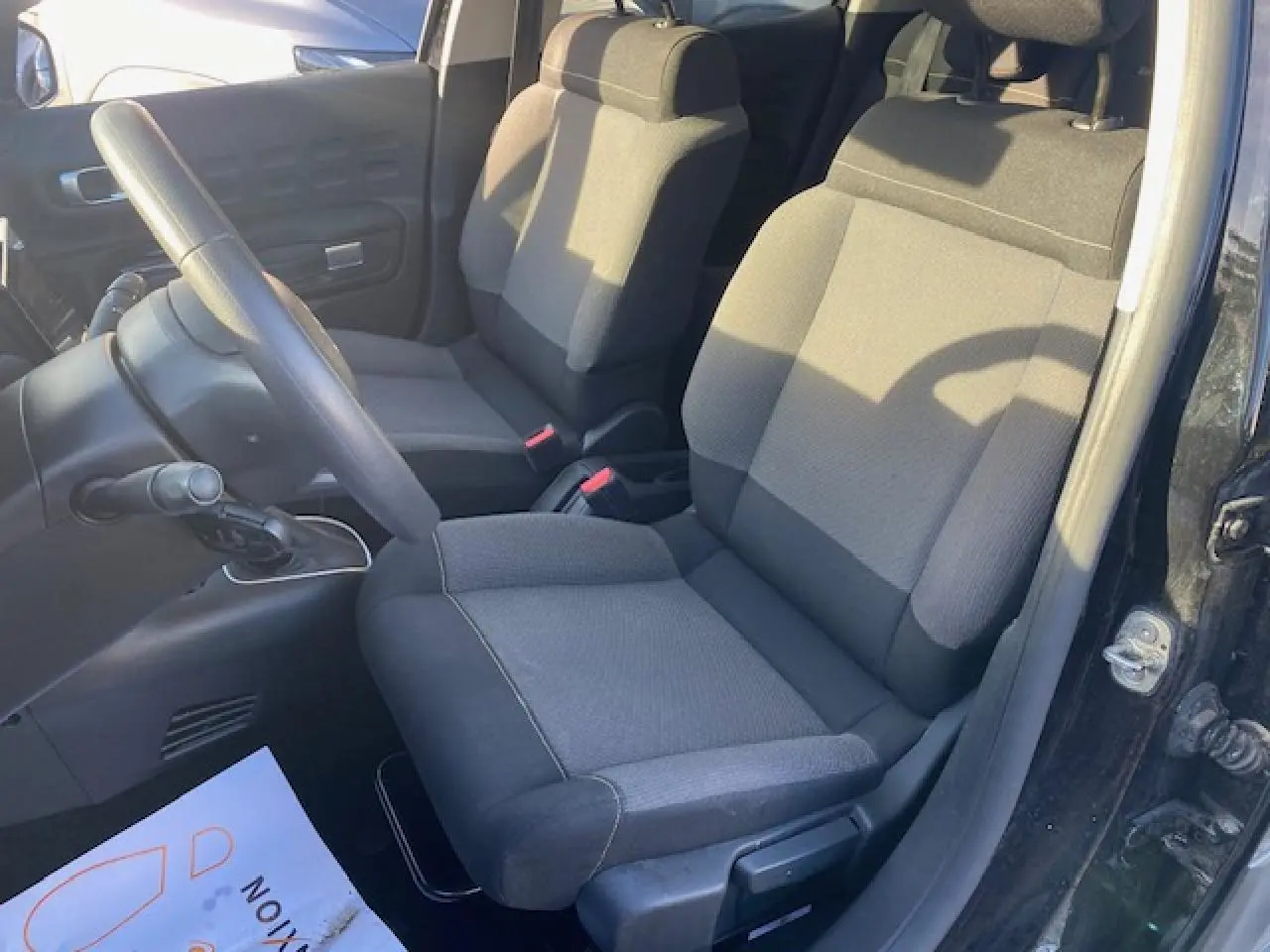 Vue intérieure côté conducteur de la Citroën C3 2023 noire, montrant les sièges en tissu et le volant simple.