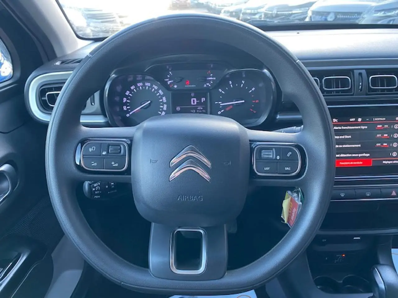 Vue centrée sur le volant de la Citroën C3 2023 noir toit rouge, avec tableau de bord et commandes au volant visibles.