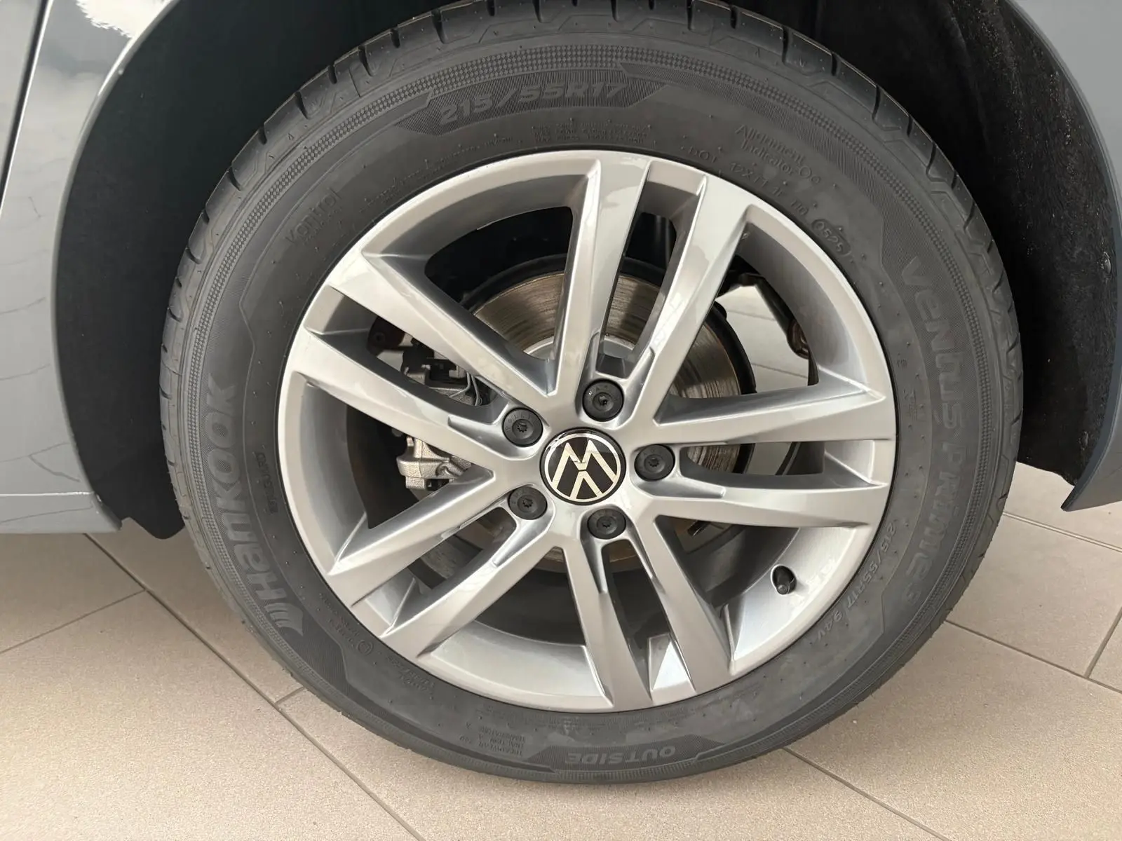 Gros plan sur la jante alliage 17 pouces avec logo VW au centre du Volkswagen Touran gris Dauphin 2025.