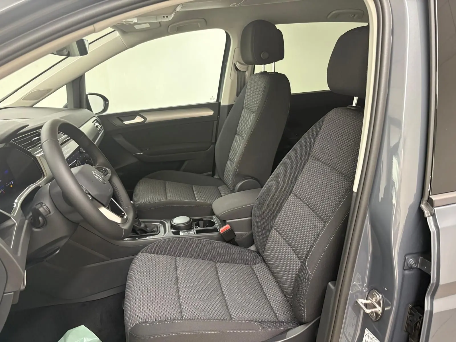 Vue intérieure côté conducteur du Volkswagen Touran gris dauphin 2025, mettant en valeur les sièges avant en tissu et le tableau de bord moderne.